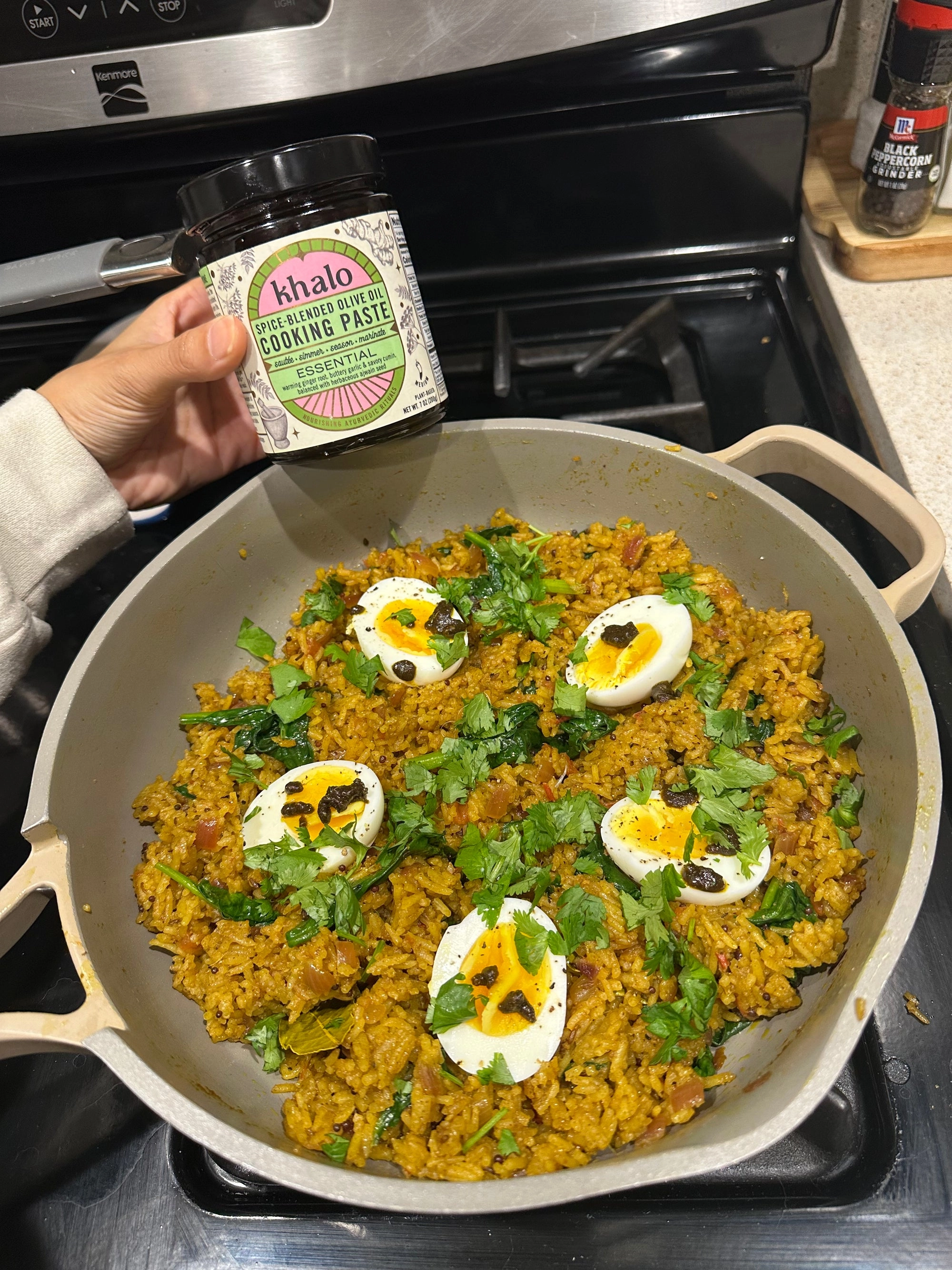 A skillet of golden rice topped with soft-boiled eggs and herbs, with a Khalo jar above