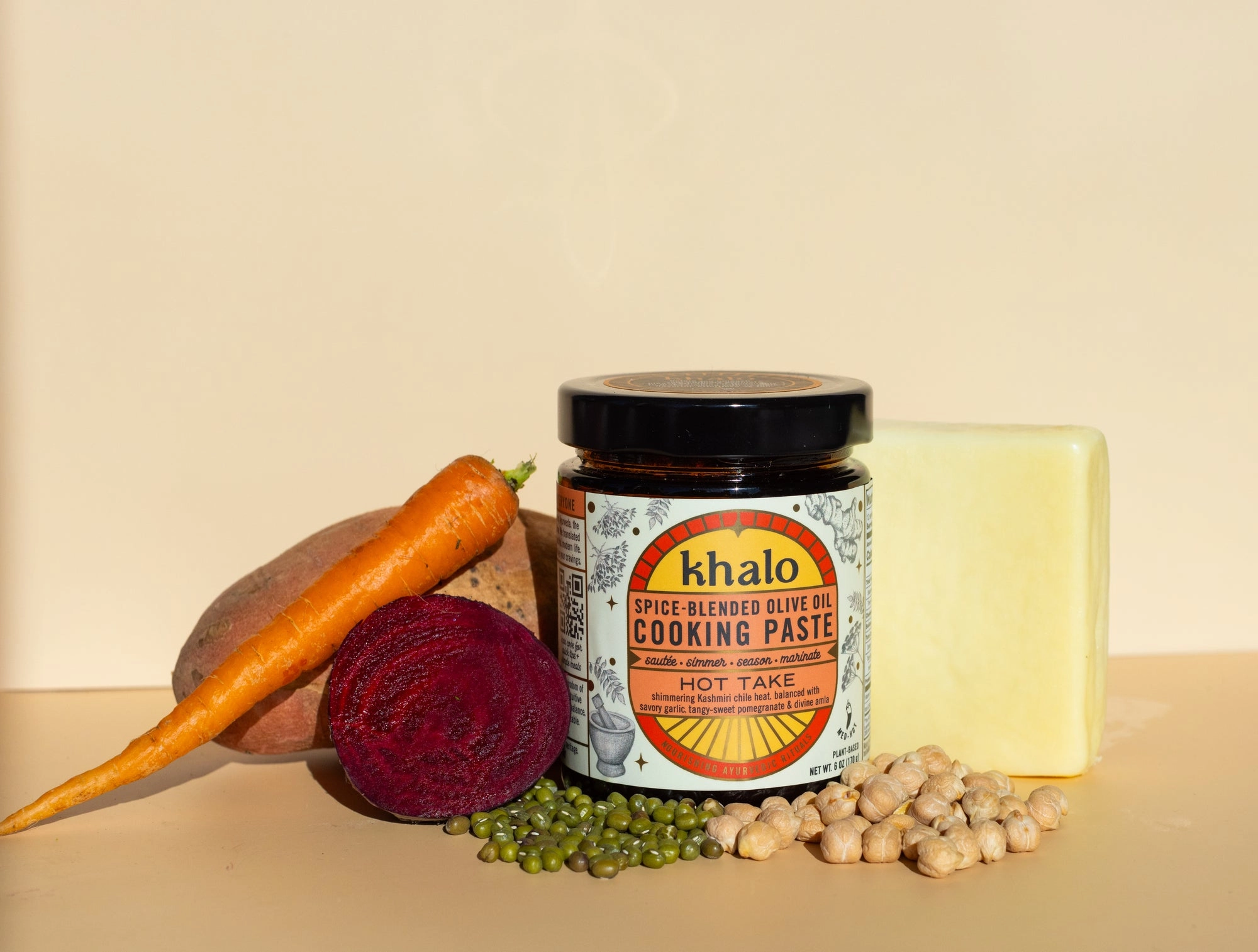 A Khalo Hot Take jar beside a carrot, a halved beet, mung beans and chickpeas