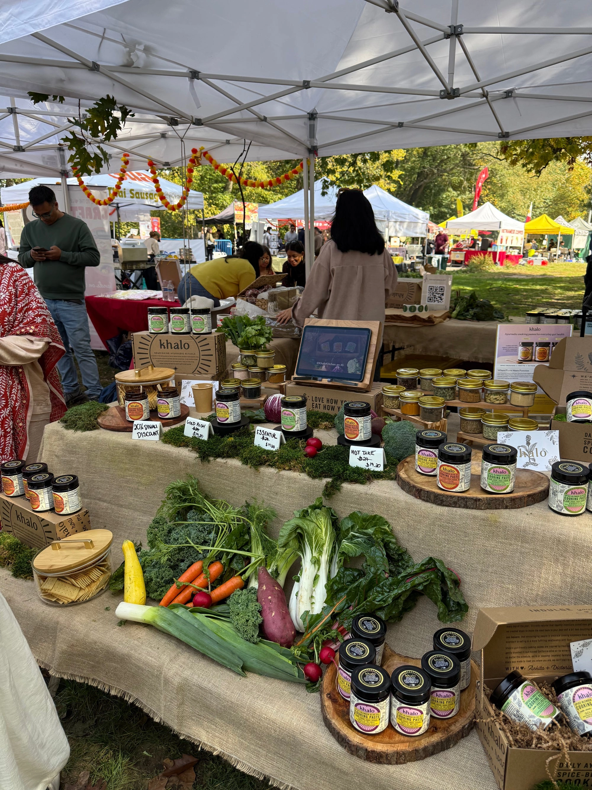 An outdoor market stall under a tent, stacked with vegetables and jars