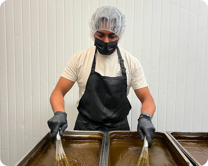 A cook in an apron and gloves stirring large trays in the Khalo kitchen