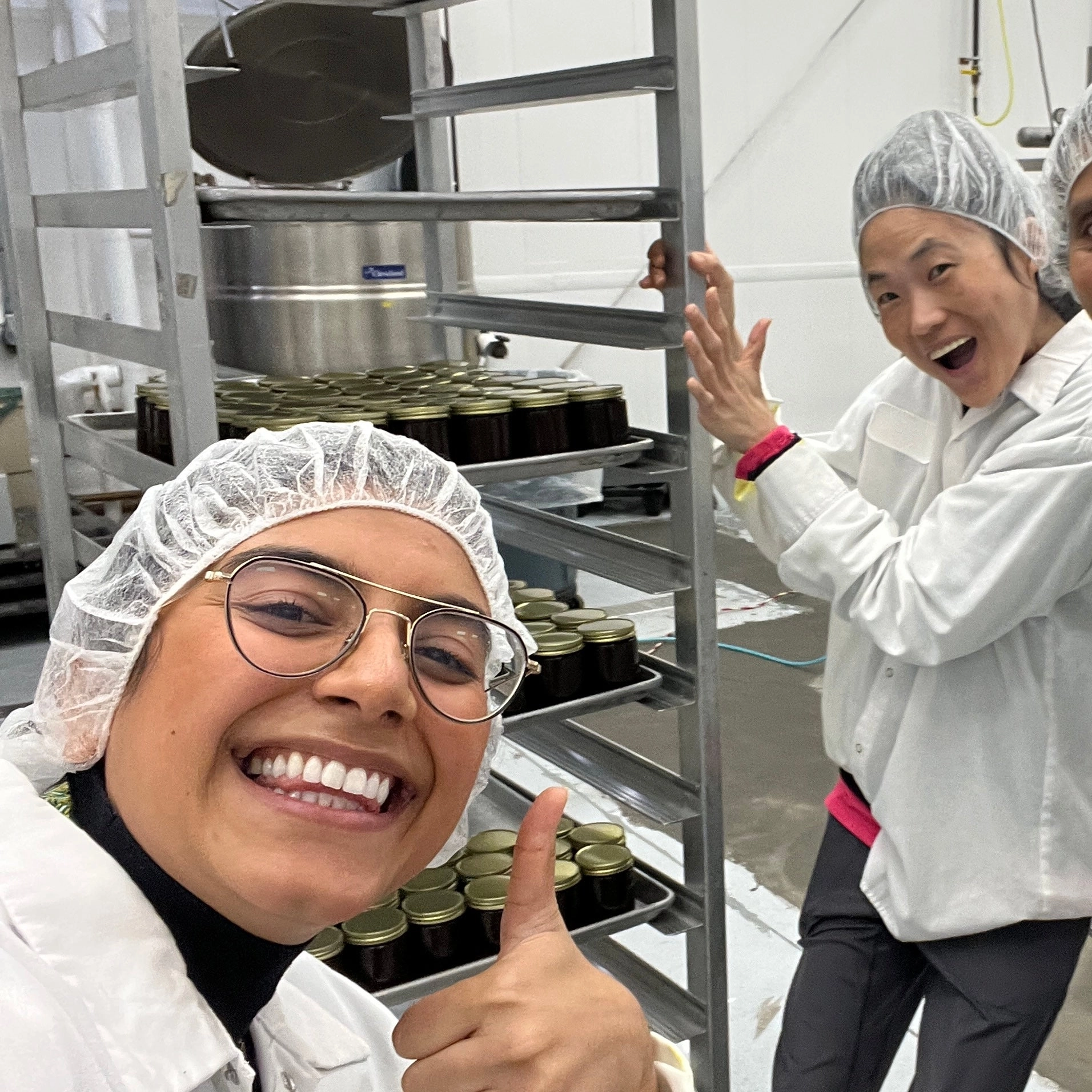 Two people in hairnets laughing and giving a thumbs up in a production kitchen