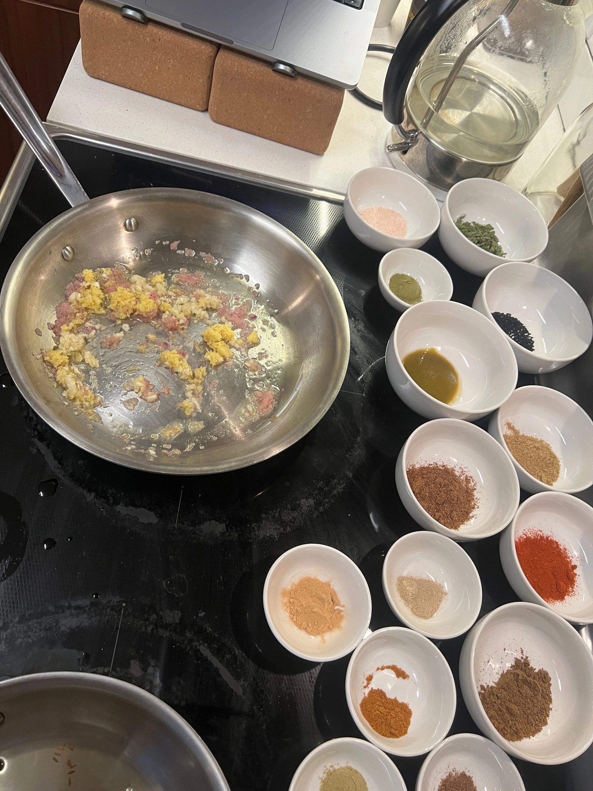 Small bowls of ground spices beside a pan on a stovetop, seen from above