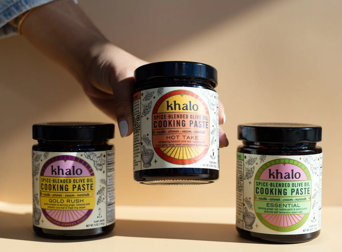 Three Khalo jars in purple, orange and green labels held together by a hand